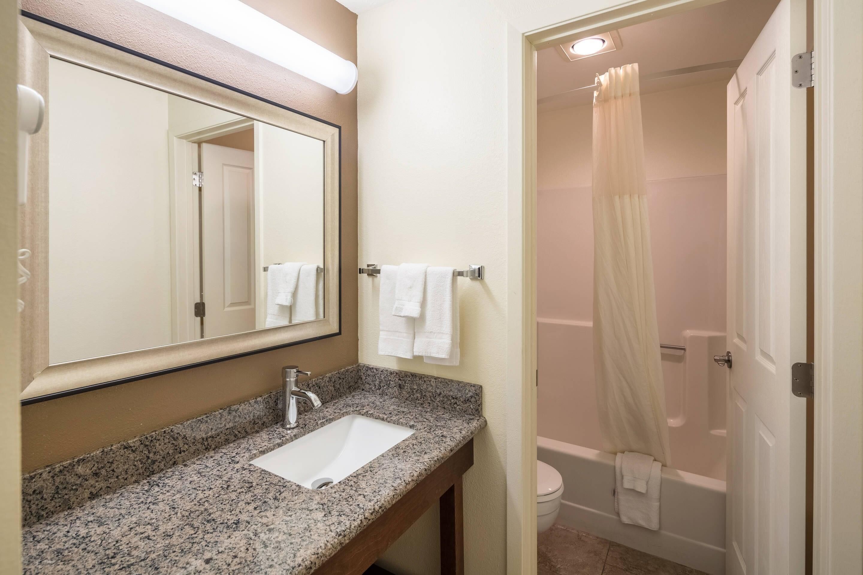 A bathroom with a granite countertop sink, a mirror, and a shower with a curtain.