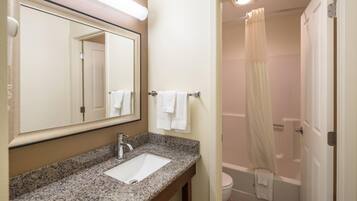 A bathroom with a granite countertop sink, a mirror, and a shower with a curtain.