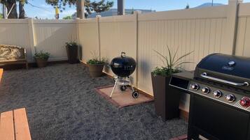 A backyard with a grill, a wooden bench, and potted plants.