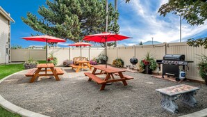 A backyard with picnic tables, red umbrellas, a barbecue grill, and a decorative table. - Quality Inn & Suites Coeur d'Alene (Coeur d'Alene)