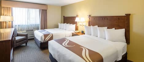 Habitación de hotel con dos camas, un escritorio, una silla y un ventanal con cortinas.