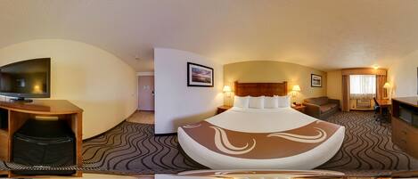 A hotel room with a large bed, a television on a wooden stand, a desk with a chair, and a microwave.