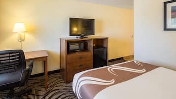 A hotel room with a bed, a desk with a lamp, a television, a microwave, and a refrigerator.