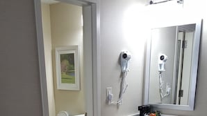 A bathroom with a white sink, a mirror, and a hairdryer mounted on the wall. - Danbury Inn & Suites (Danbury)