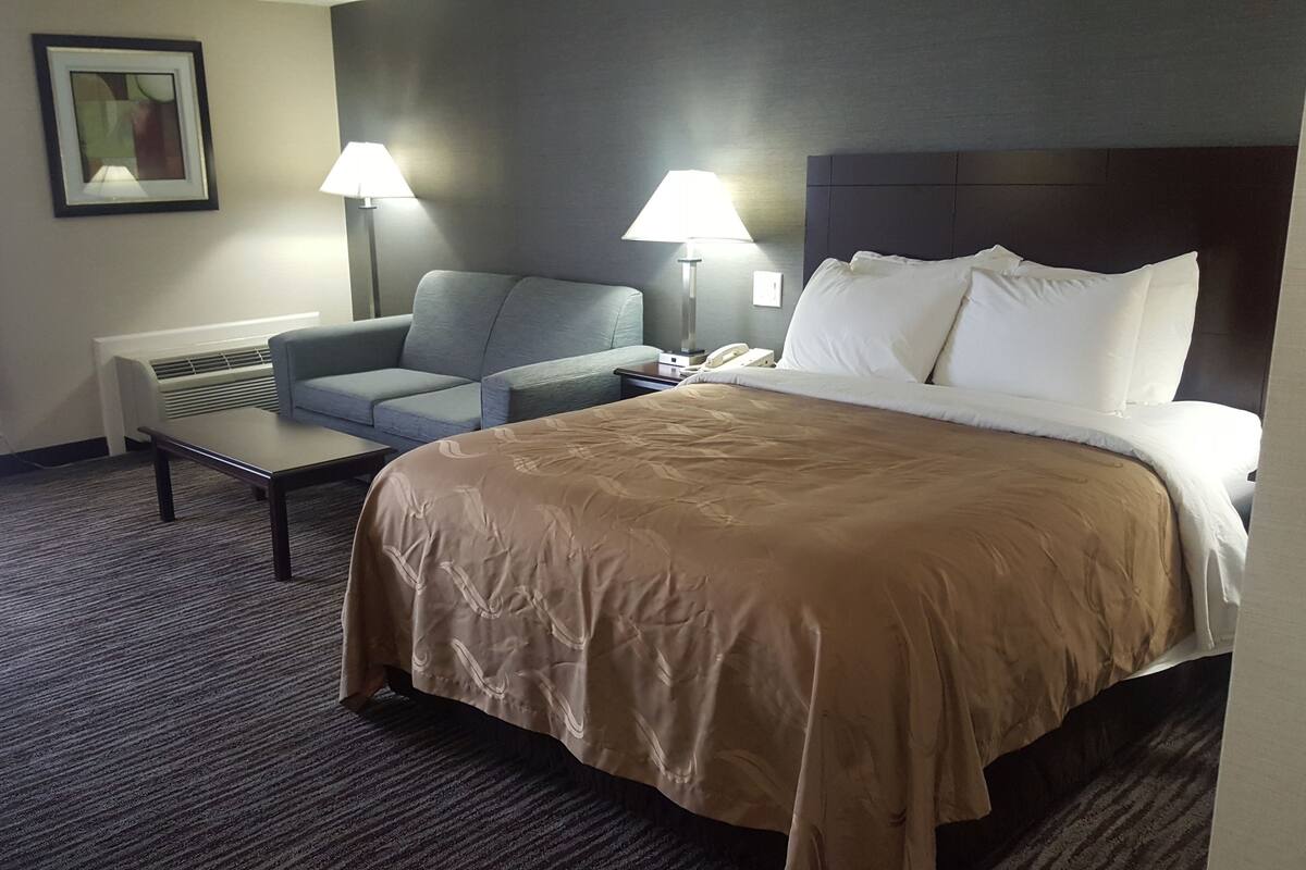 A hotel room with a bed, a desk, a chair, two lamps, and a picture on the wall.