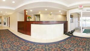 A hotel reception area with a wooden reception desk, a carpeted floor, and an exit sign.