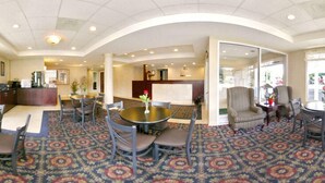 A hotel lobby with a round dining table, several chairs, a reception desk, and a patterned carpet.