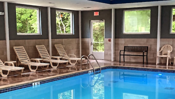 An indoor swimming pool with clear blue water, surrounded by lounge chairs and a bench. - Danbury Inn & Suites (Danbury)