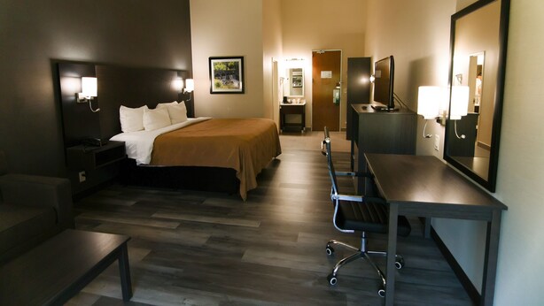 A hotel room with a bed, bedside table, desk, chair, and a mirror. - Danbury Inn & Suites (Danbury)