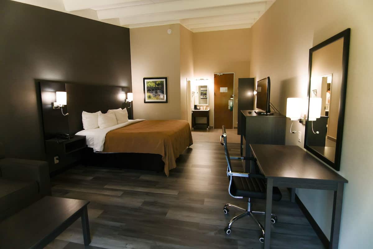 A hotel room with a bed, bedside table, desk, chair, and a mirror.