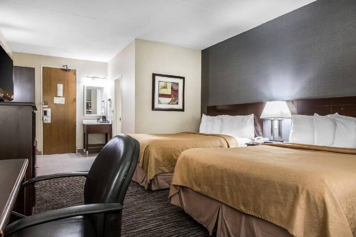A hotel room with two beds, a desk, a chair, a mirror, and a framed picture on the wall.