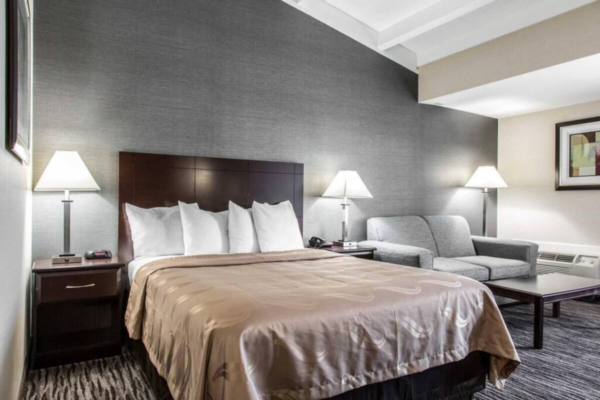 Una habitación de hotel con una cama grande, dos mesitas de noche, un sofá y un escritorio.