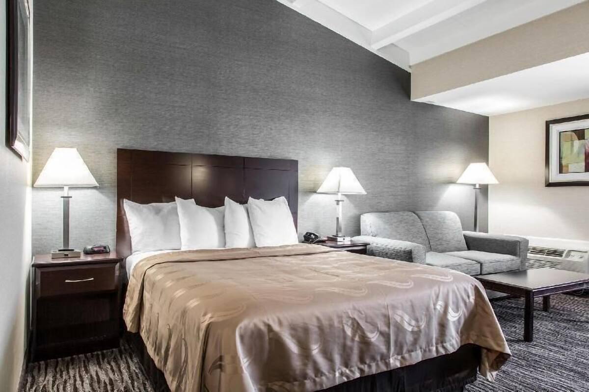 A hotel room with a bed, two bedside lamps, a sofa, a coffee table, and a framed picture on the wall.