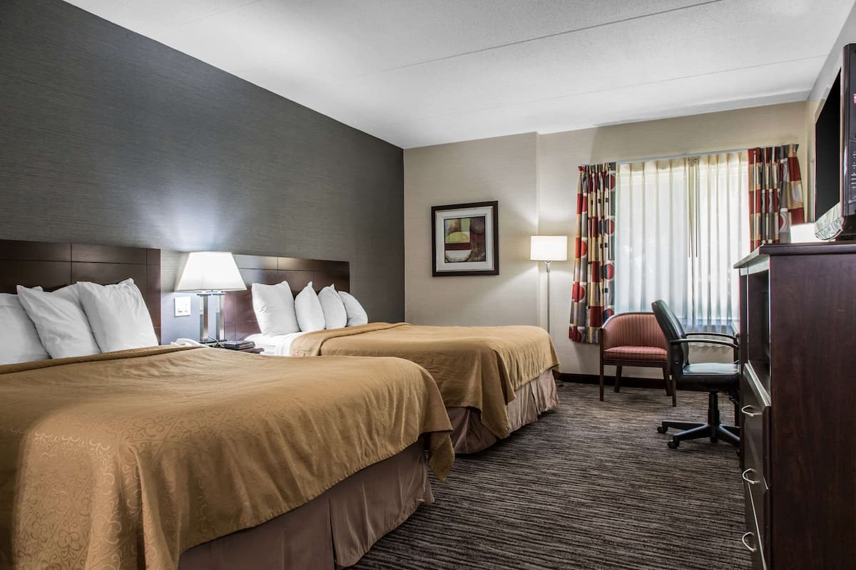 A hotel room with two beds, a desk, a chair, a TV, and a window with curtains.