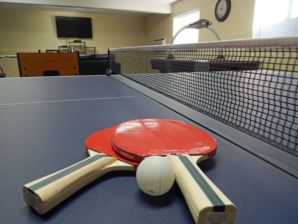 Enjoy a game of table tennis in this hotel room, featuring a table with a net, paddles, and a ball.