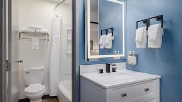 A modern bathroom with a white toilet, a bathtub, a white sink with a mirror, and towels on a rack.