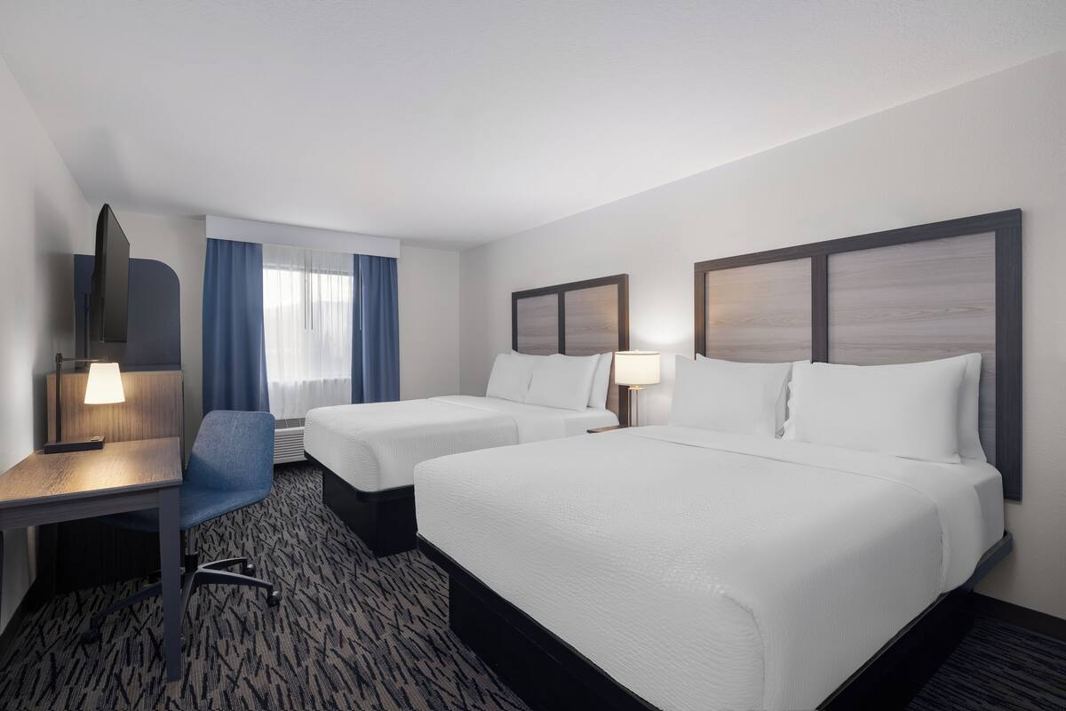 A hotel room with two beds, a desk, a chair, and a large mirror.