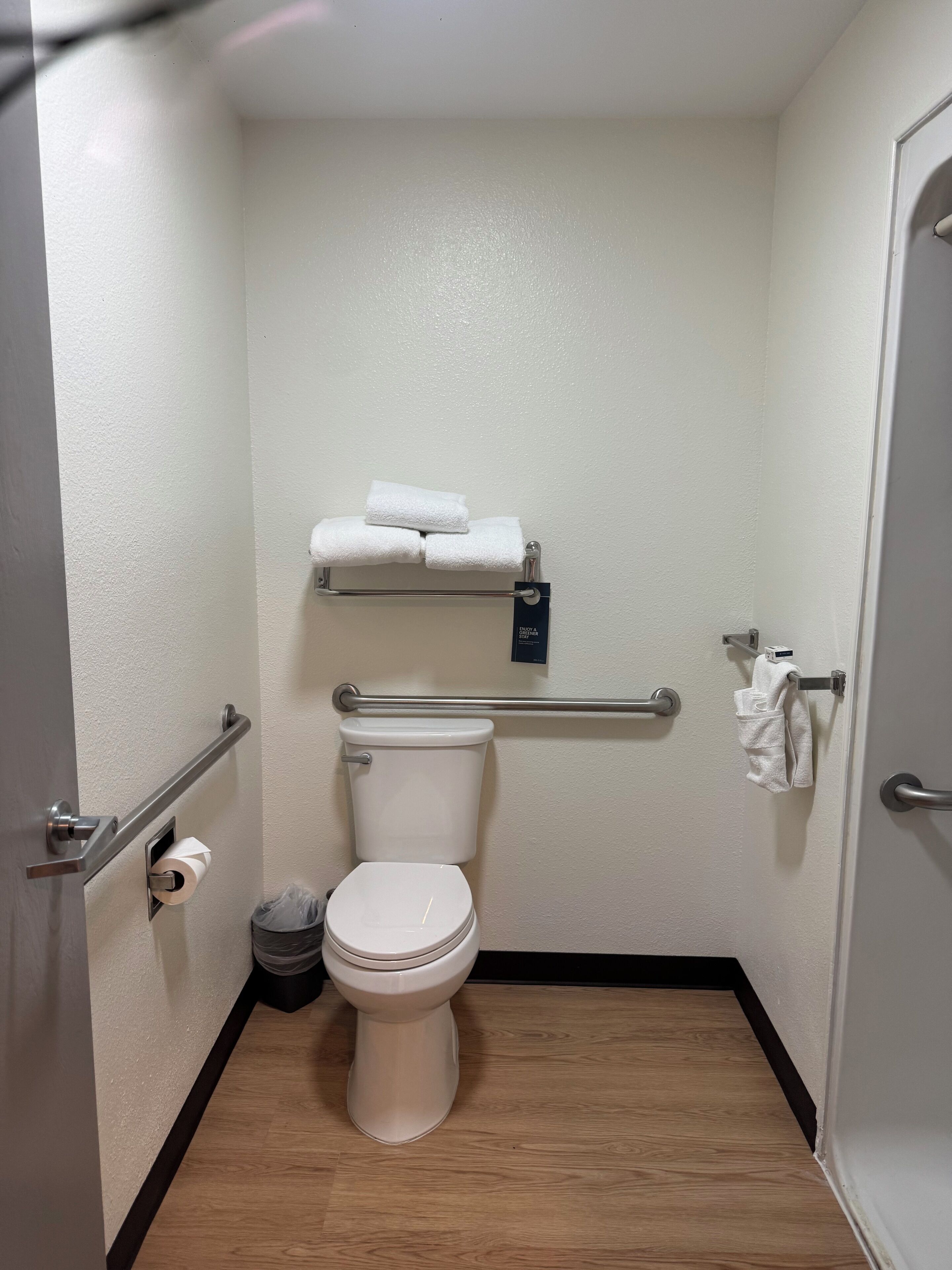 Ein kleines, sauberes Badezimmer mit Toilette, Handtrockner, Mülleimer und Handtuchhalter.