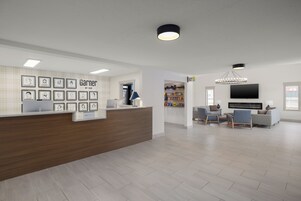 A modern reception area with a wooden counter, framed artwork, a television, and a seating area with sofas and chairs.