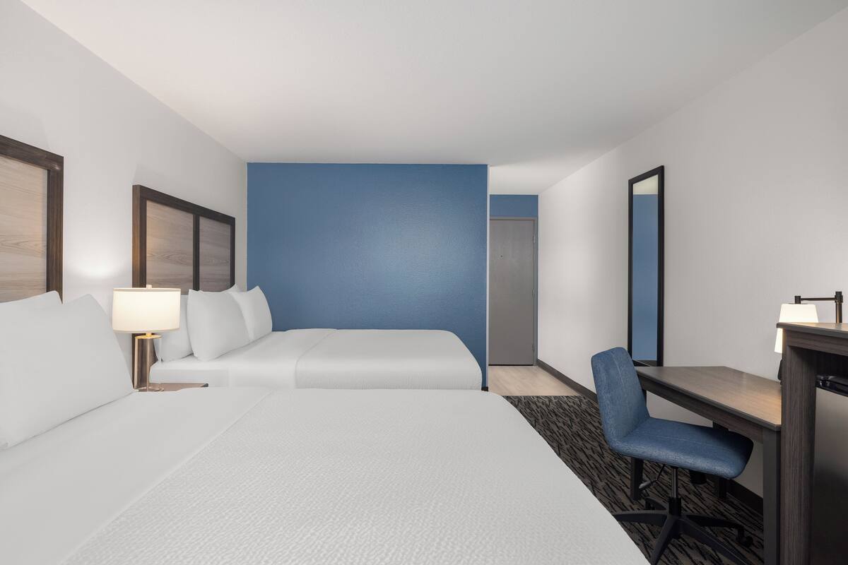 Una habitación de hotel con cama, escritorio, silla, lámpara y espejo.