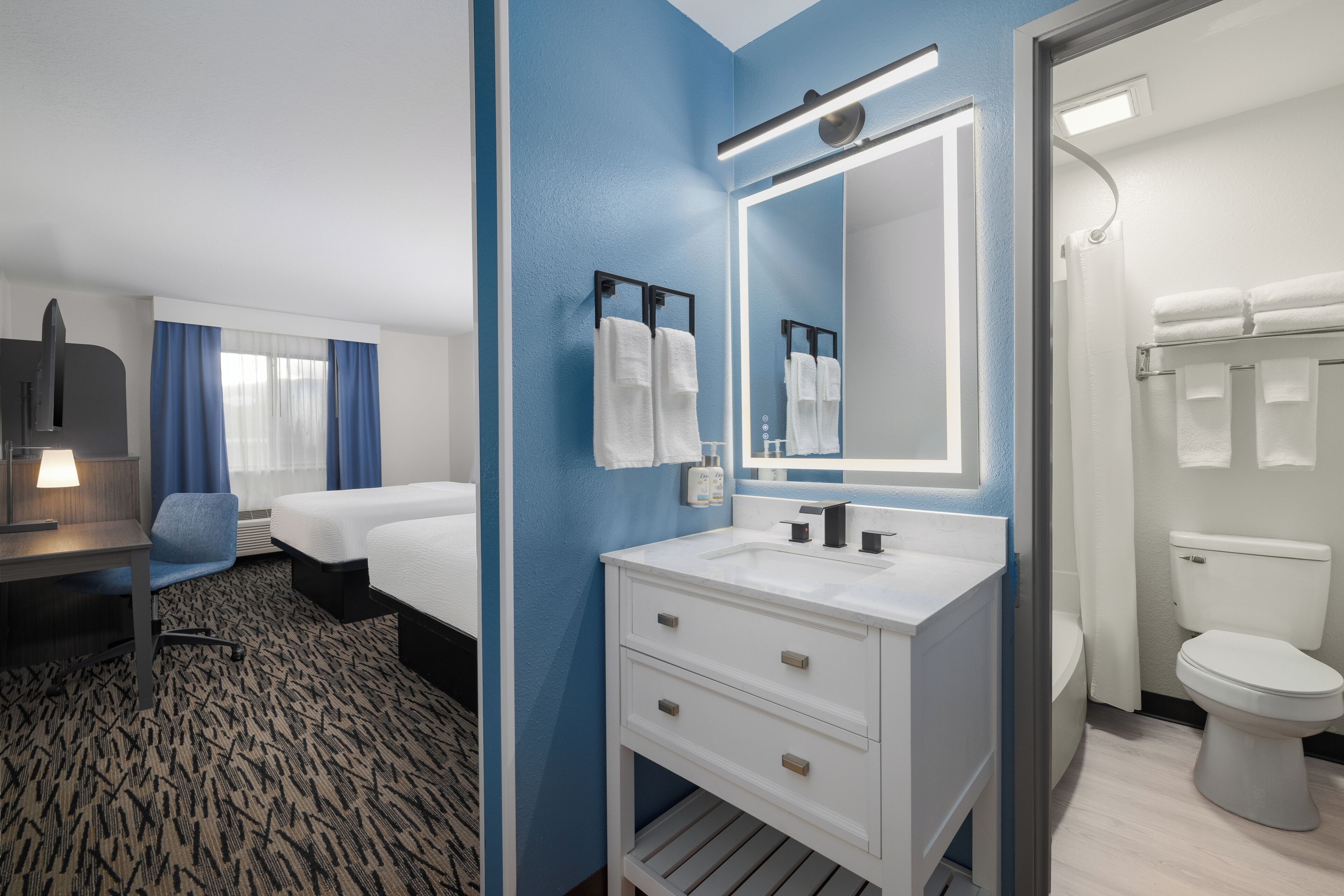 Ein Hotelzimmer mit Bett, Schreibtisch, Badezimmer mit Waschbecken und Spiegel sowie Toilette.
