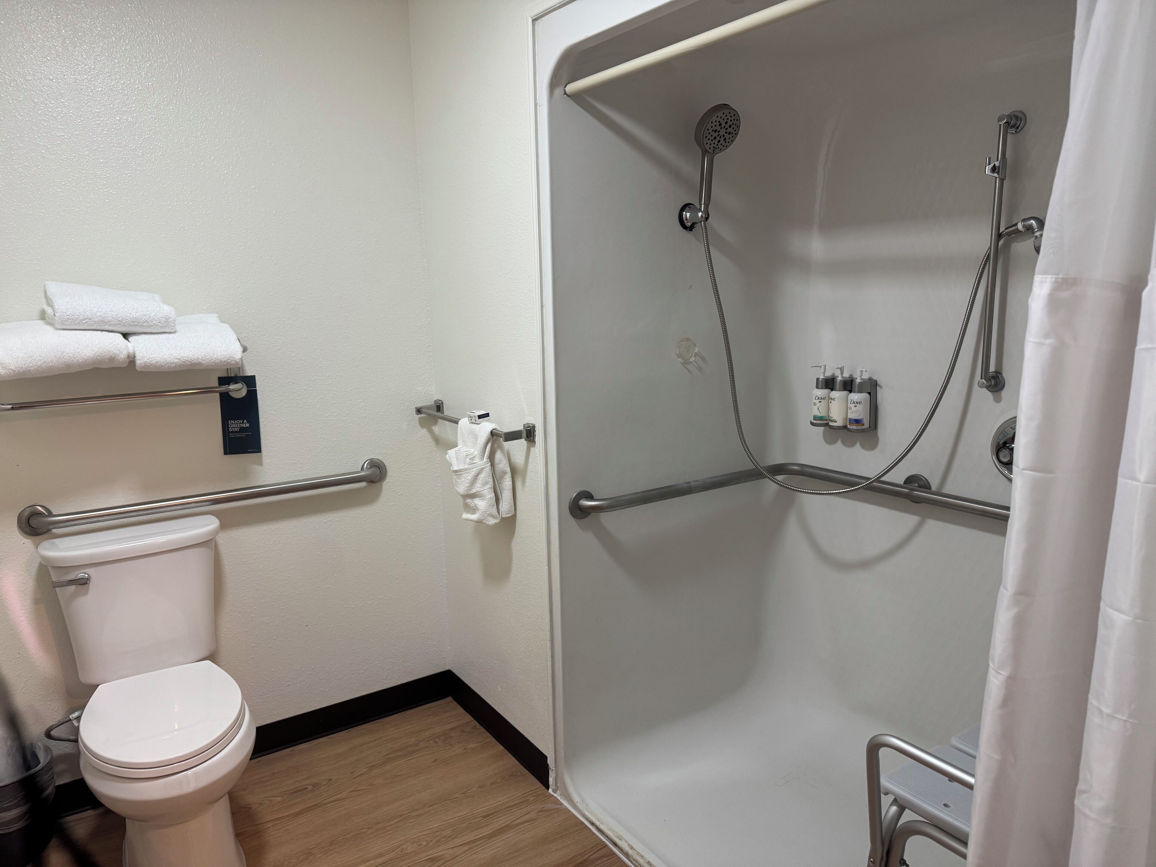 Een badkamer met een toilet, een douche met handgrepen en een handdoekrek met handdoeken.