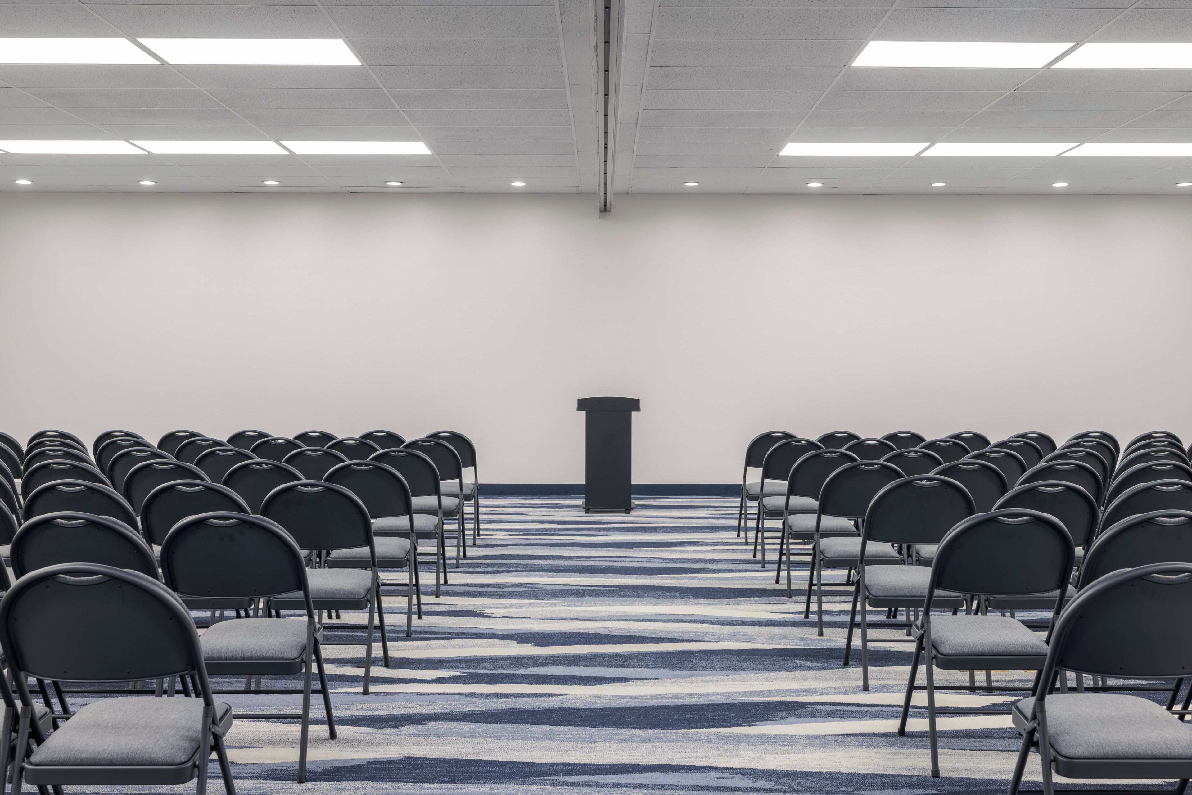A conference room with rows of chairs, a podium, and a patterned carpet.