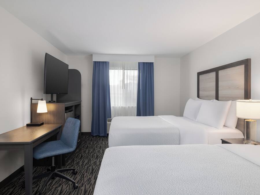 A hotel room with two beds, a desk, a TV, and a window with curtains.