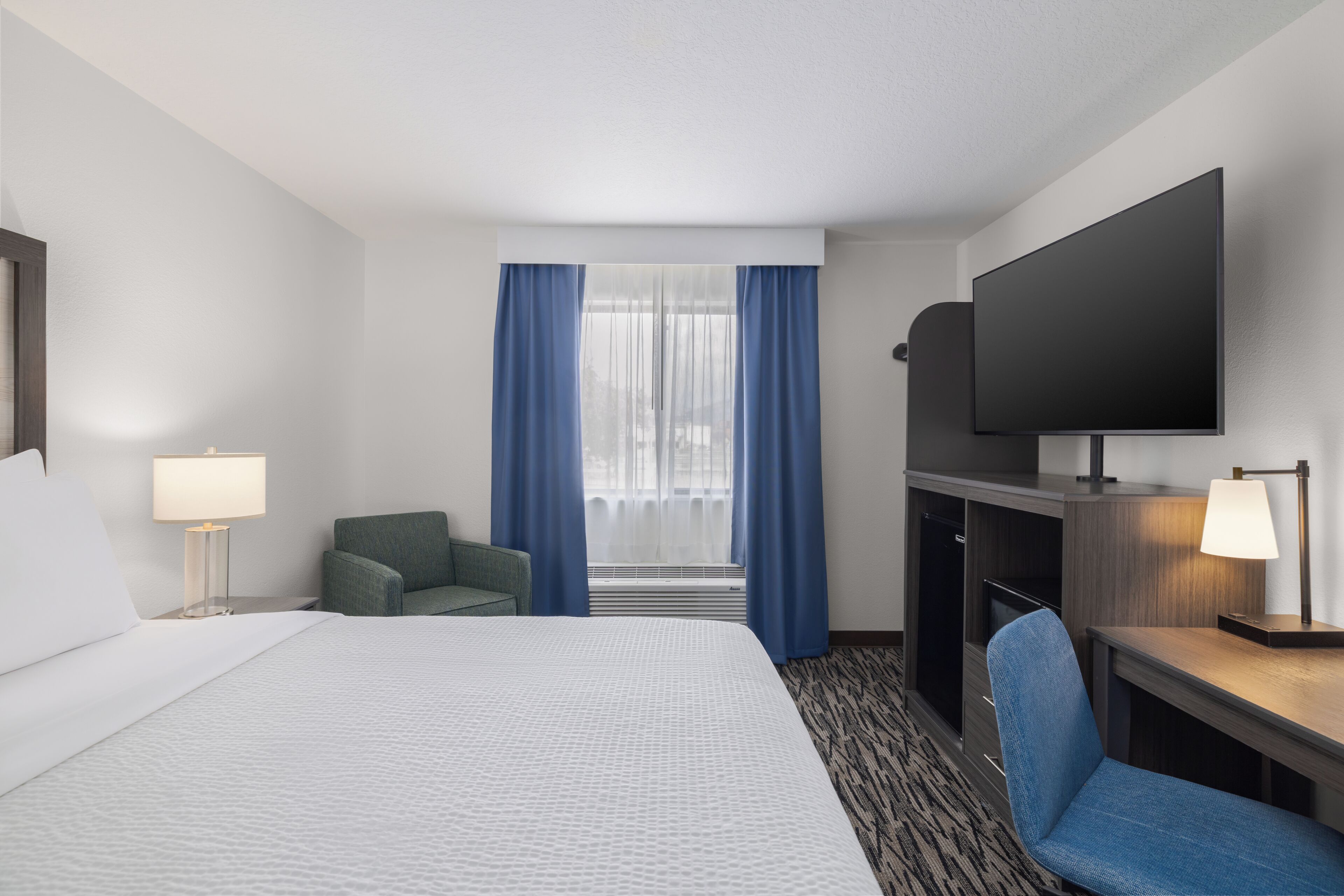 A hotel room with a bed, a desk, a chair, a television, and a window with curtains.