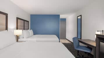 A hotel room with a bed, a desk, a chair, a lamp, and a mirror.
