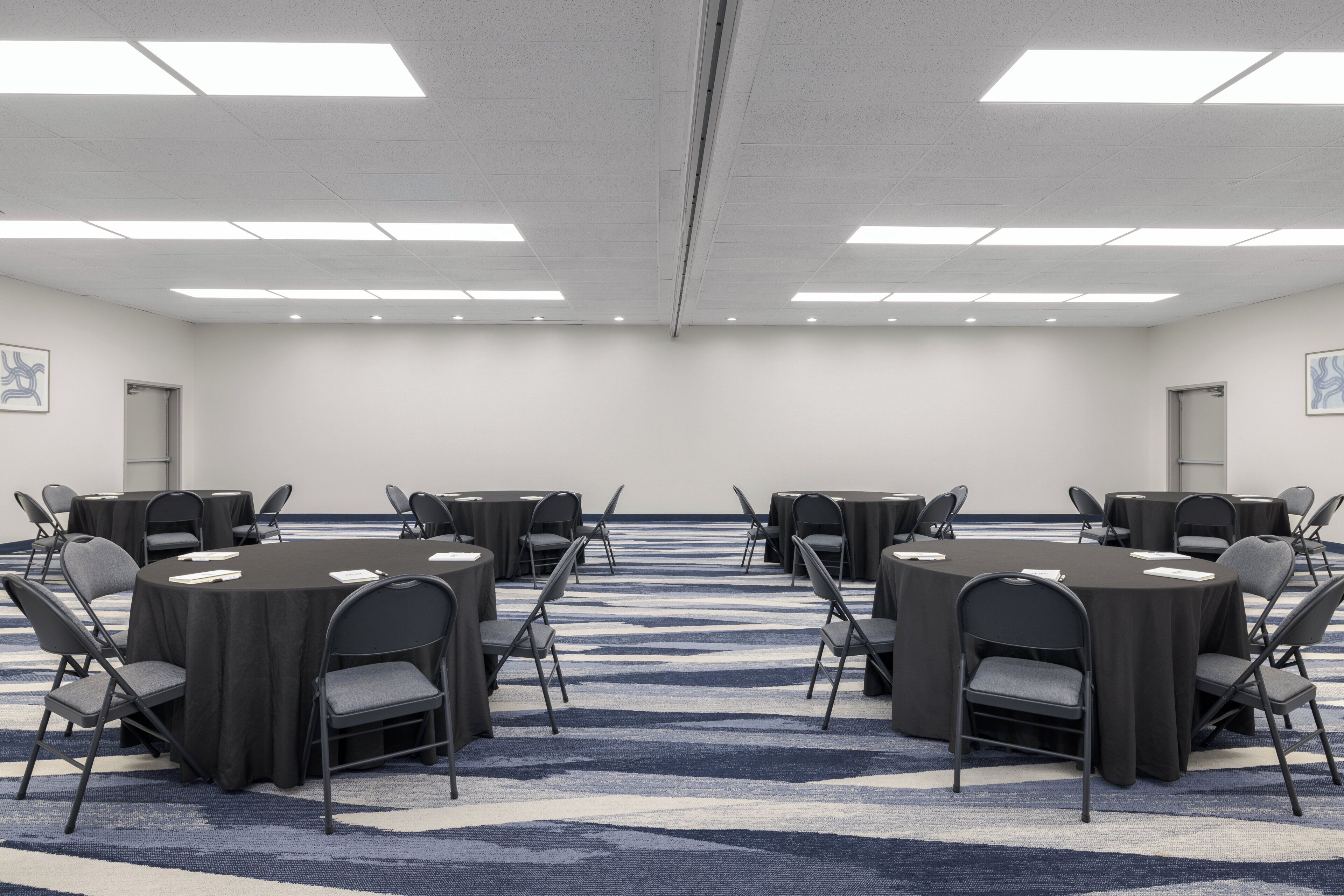 A conference room with round tables, chairs, and a carpeted floor.
