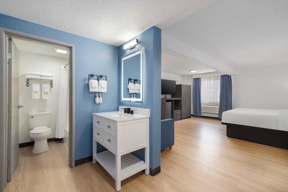 A hotel room with a bathroom, a bed, a TV, and a window with curtains.