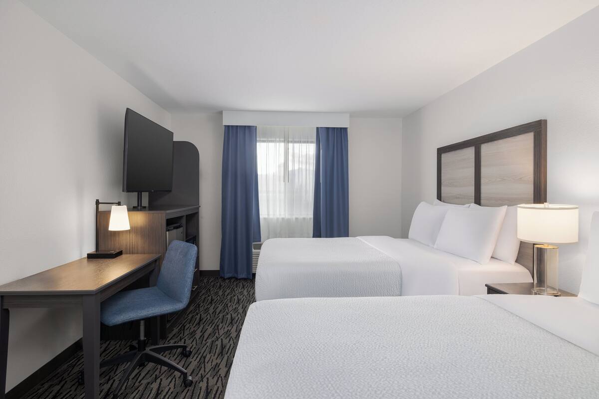 Una habitación de hotel con dos camas, un escritorio con una silla, un televisor y una ventana con cortinas.