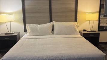 Une chambre d’hôtel avec un grand lit, deux tables de chevet avec des lampes, une tête de lit en bois et un sol recouvert de moquette.