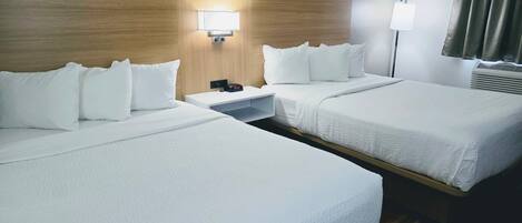 Una habitación de hotel con dos camas, una mesita de noche, una lámpara y un ventanal con cortinas.