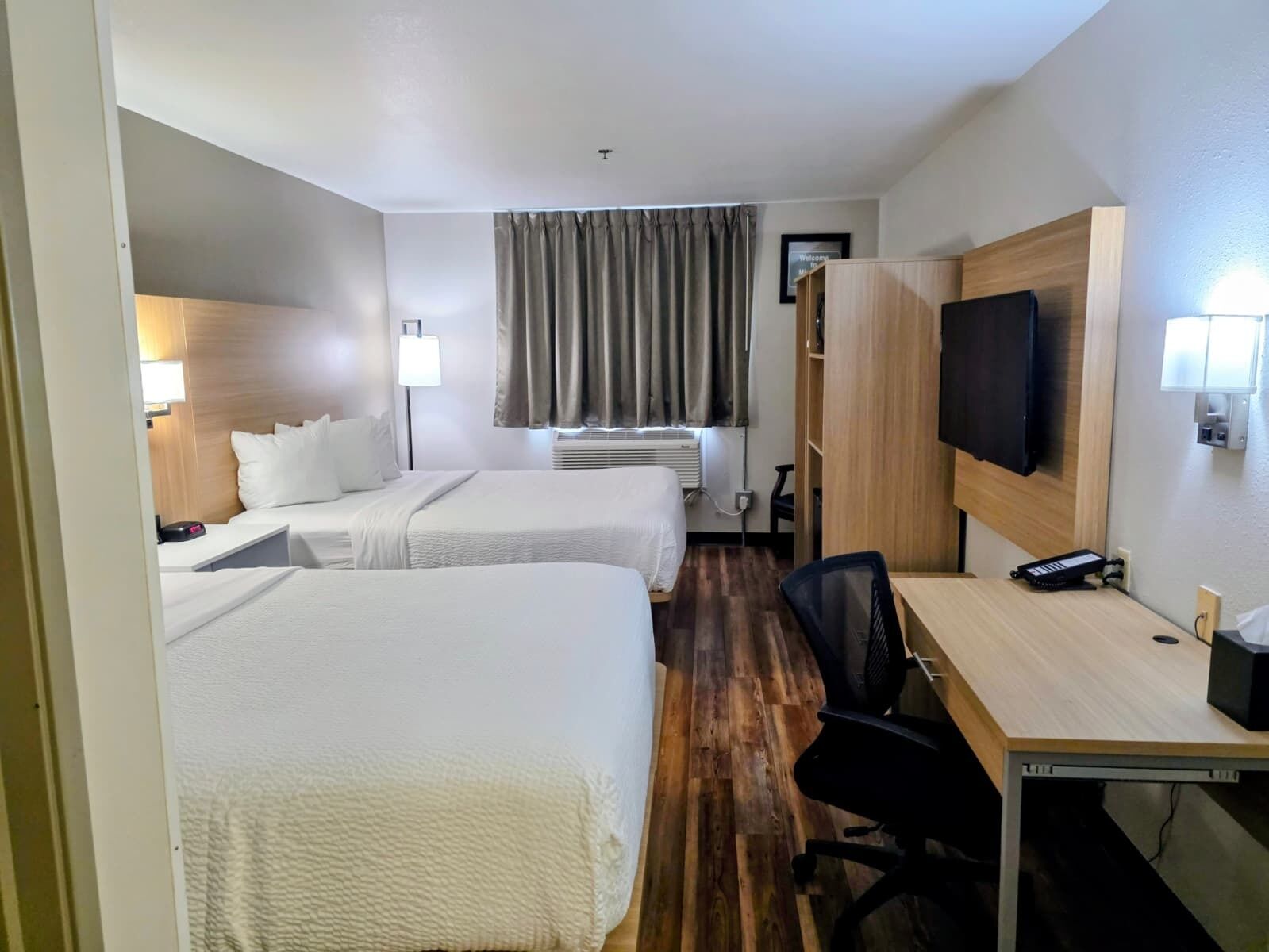 Une chambre d’hôtel avec deux lits, un bureau, une chaise, une télévision et une fenêtre avec des rideaux.