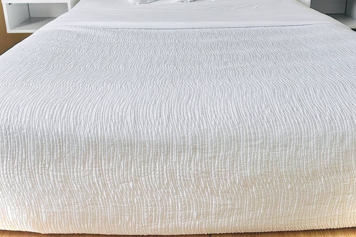 A neatly made bed with a textured white duvet, wooden headboard, and bedside tables with clocks.