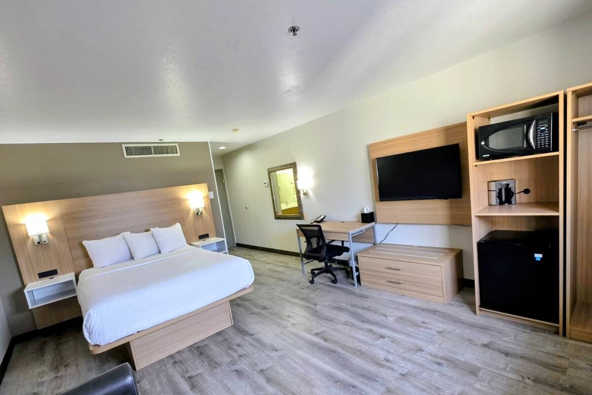 A hotel room with a bed, desk, chair, wardrobe, and a TV.
