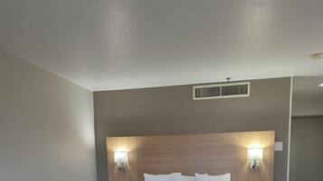 Une chambre d’hôtel avec un grand lit, deux tables de chevet avec des lampes, une tête de lit en bois et une grille d’aération au plafond.