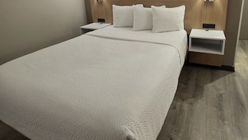 A neatly made bed with a white duvet, two bedside tables with lamps, and a wooden headboard.