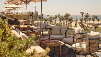 A terrace with wicker furniture, umbrellas, and a view of the beach.