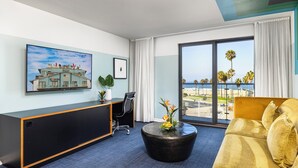 A hotel room with a large window, a sofa, a desk with a chair, and a painting on the wall. - Hotel Erwin Venice Beach (Venice)