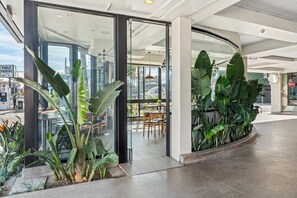 A modern indoor space with glass doors leading to an outdoor seating area, surrounded by large green plants. - Hotel Erwin Venice Beach (Venice)