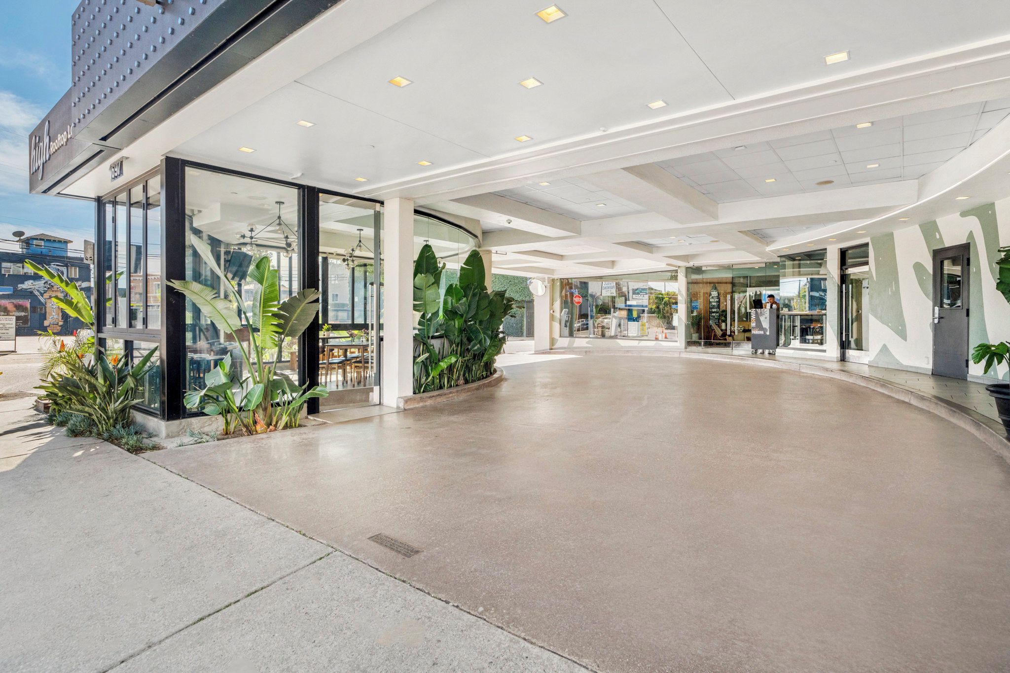 A modern hotel entrance with a curved concrete floor, glass doors, and indoor plants.