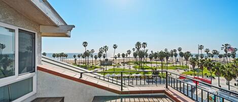 A balcony with a view of a beach, palm trees, and a clear sky.