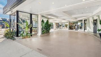 A modern hotel entrance with a glass facade, indoor plants, and a clean, spacious lobby area.