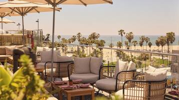 A terrace with wicker furniture, a table set for dining, and a view of the beach and palm trees.