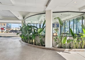 A modern building entrance with a curved glass facade, large green plants, and a visible exit sign. - Hotel Erwin Venice Beach (Venice)