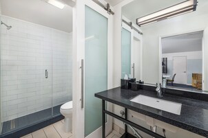 Un baño moderno con cabina de ducha de vidrio, inodoro blanco, lavamanos con encimera negra y un espejo grande.