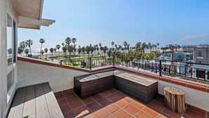 A balcony with a wooden bench, a small table, and a view of the beach and palm trees. - Hotel Erwin Venice Beach (Venice)
